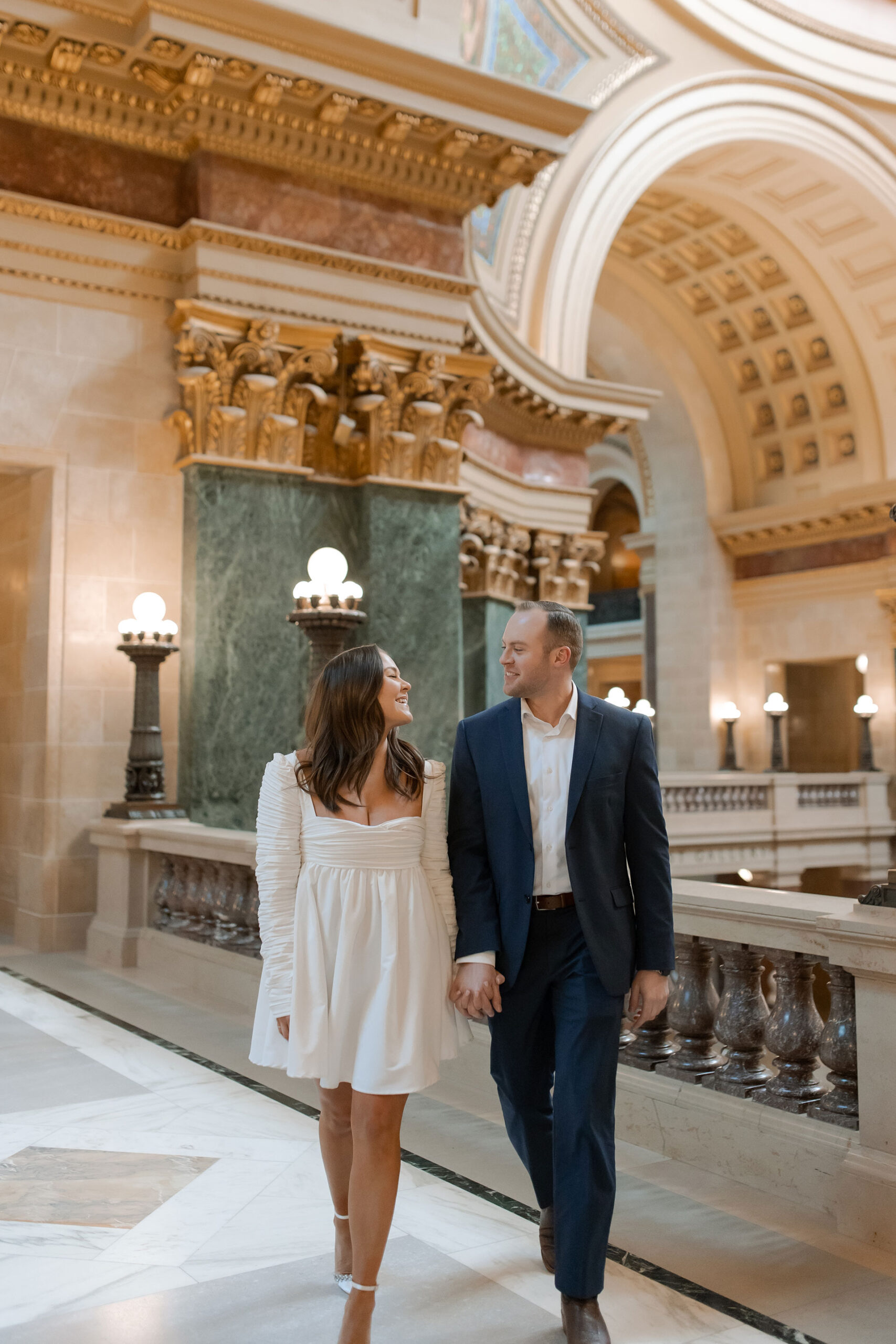 A couple in a suit + white dress take engagement photos in the Wisconsin State Capitol by Claire Neville Photography 