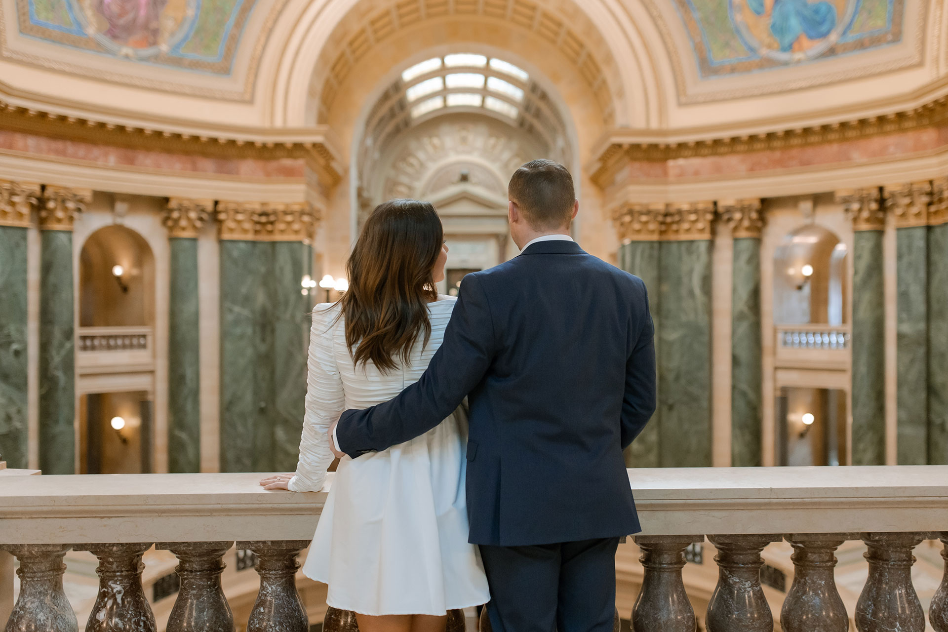 A couple in a suit + white dress take engagement photos in the Wisconsin State Capitol by Claire Neville Photography 