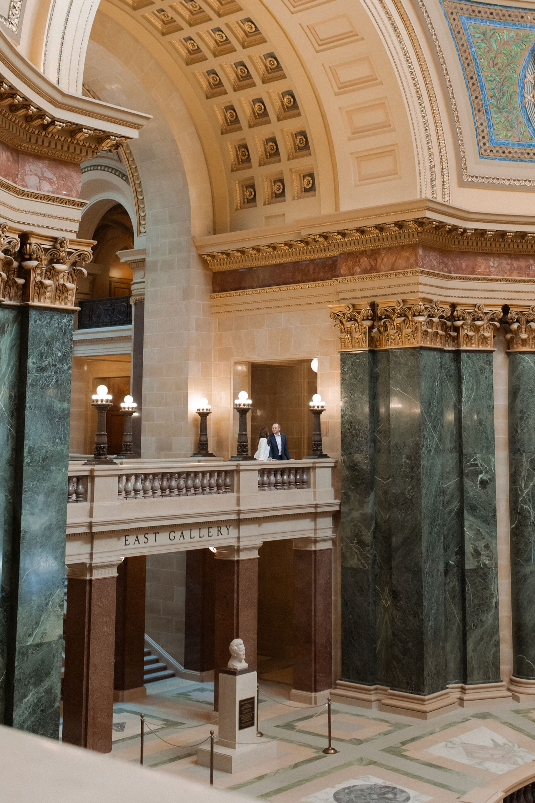 A couple in a suit + white dress take engagement photos in the Wisconsin State Capitol by Claire Neville Photography 