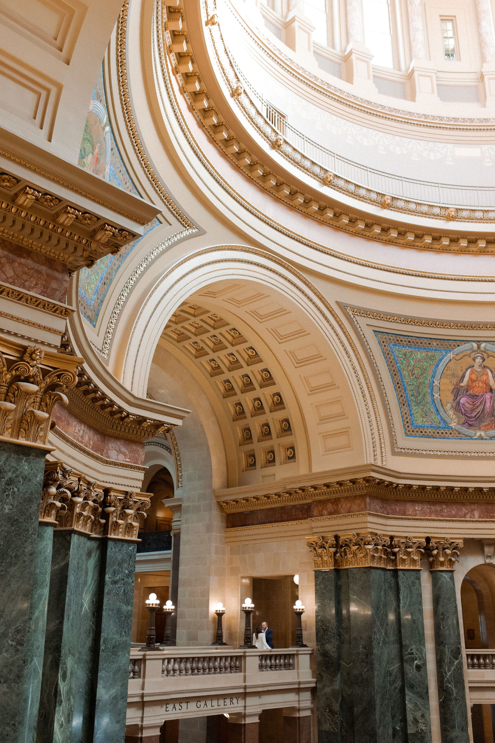 A couple in a suit + white dress take engagement photos in the Wisconsin State Capitol by Claire Neville Photography 