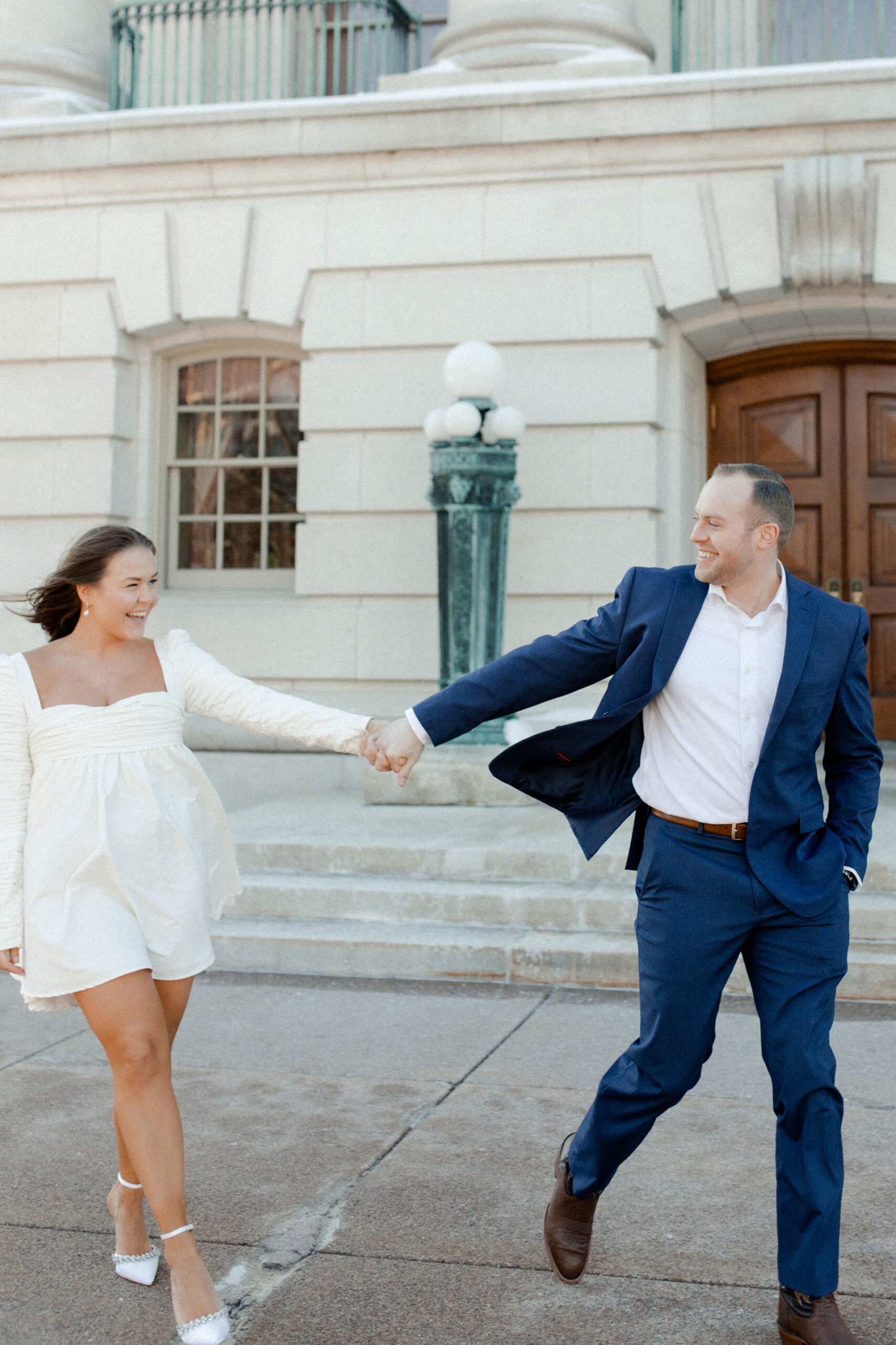 A couple in a suit + white dress take engagement photos outside the Wisconsin State Capitol by Claire Neville Photography 