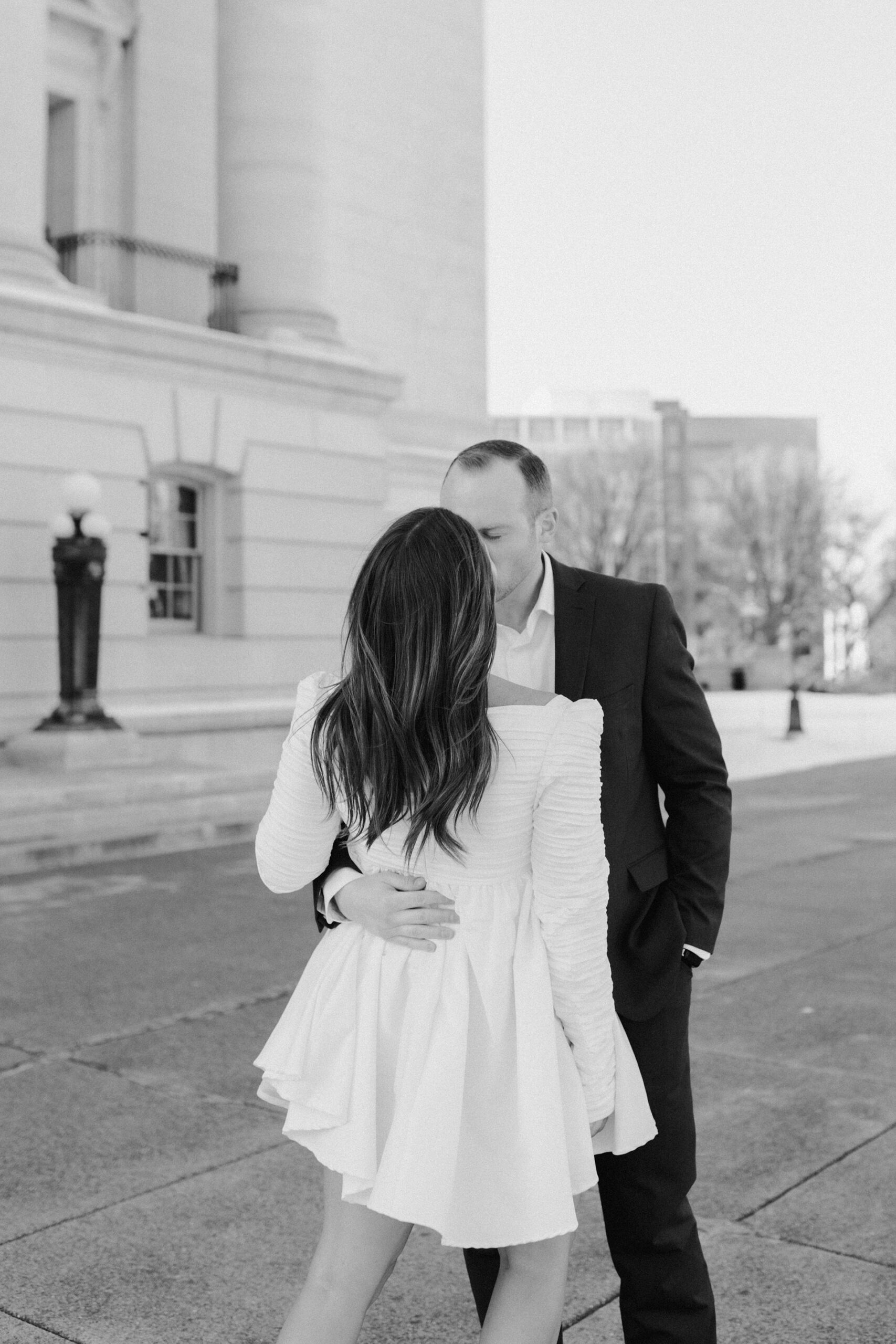 A couple in a suit + white dress take engagement photos outside the Wisconsin State Capitol by Claire Neville Photography 