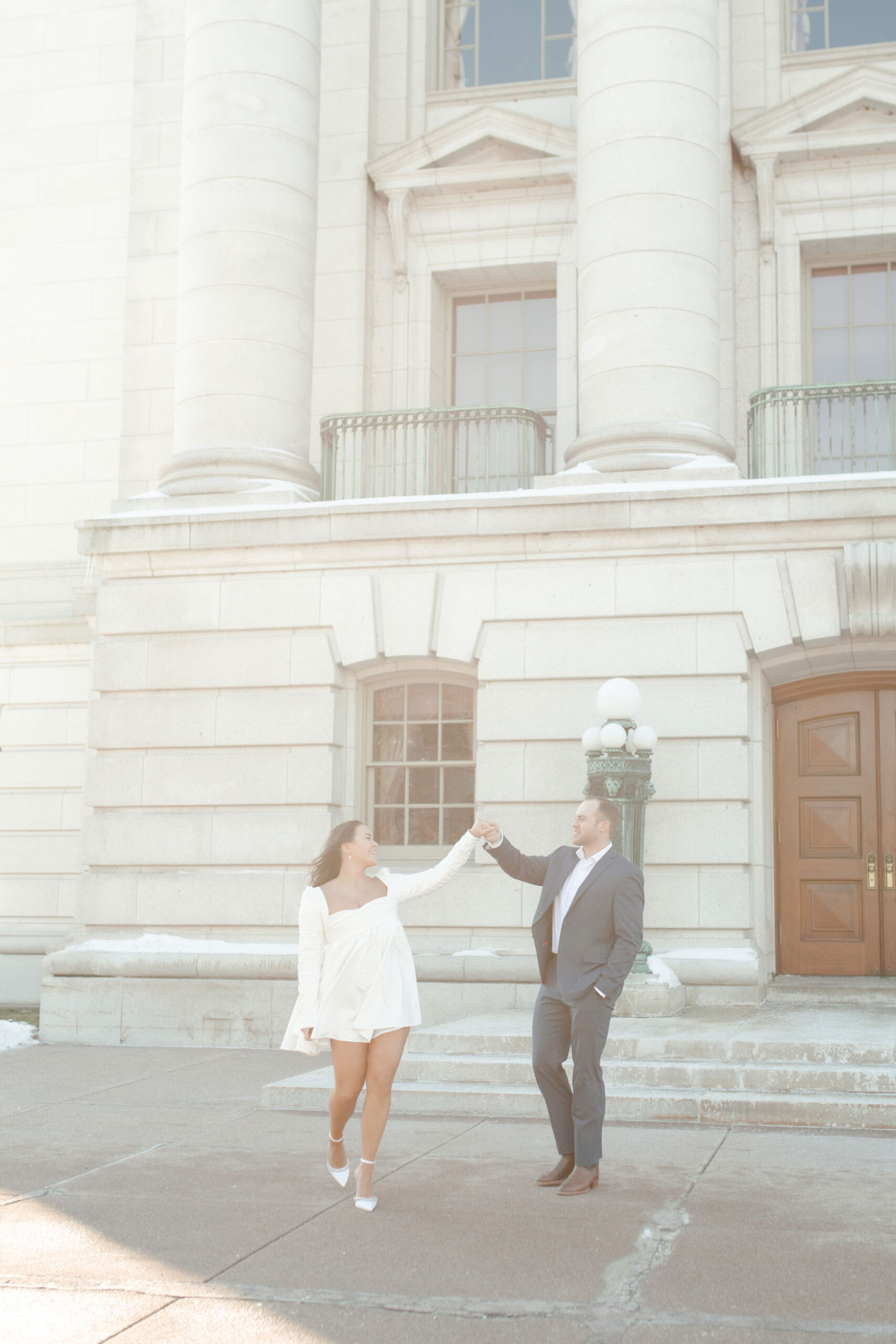 A couple in a suit + white dress take engagement photos outside the Wisconsin State Capitol by Claire Neville Photography 