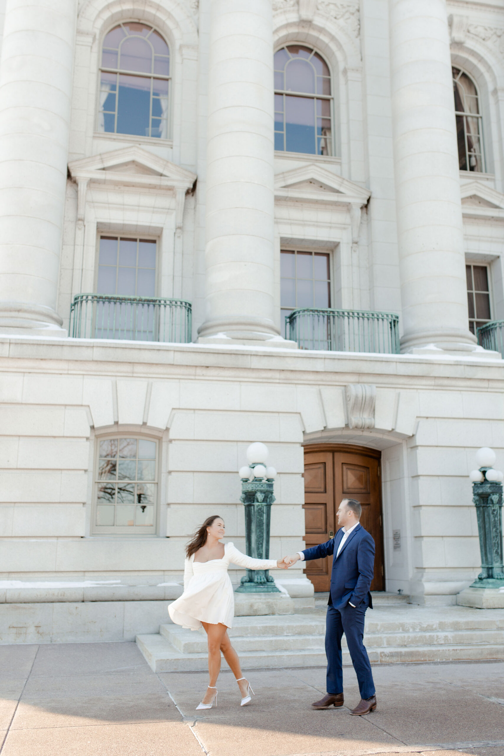 A couple in a suit + white dress take engagement photos outside the Wisconsin State Capitol by Claire Neville Photography 