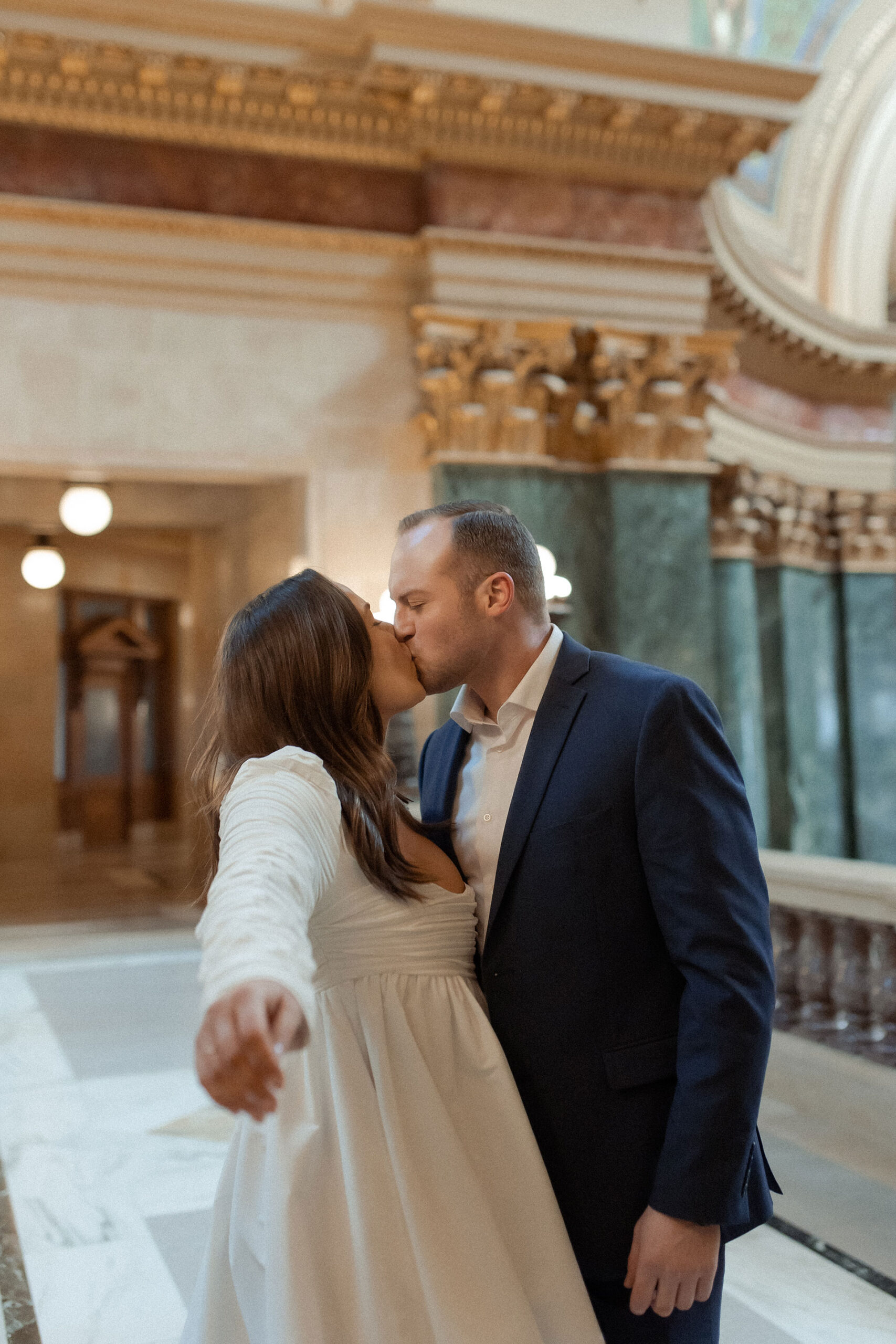 A couple in a suit + white dress take engagement photos in the Wisconsin State Capitol by Claire Neville Photography 