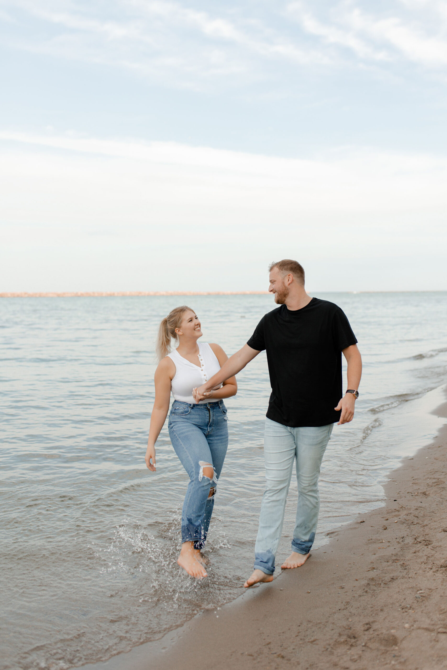 A couple along the beach in milwaukee posing for engagement photos that are documentary style captured by Claire Neville Photography